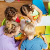 Drei Kinder sitzen zusammen mit einer Kindergärtnerin an einem Tisch und basteln.